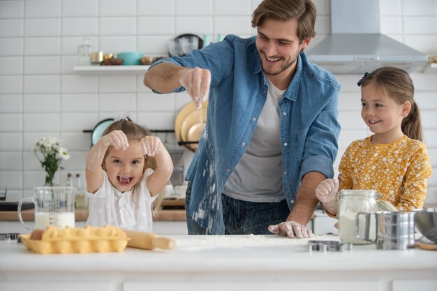 Foto di un padre e delle figlie sorridenti che cucinano in cucina e si divertono.