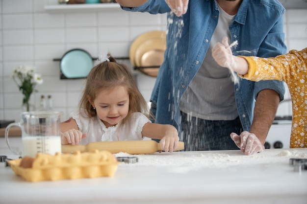 Foto di un padre e delle figlie sorridenti che cucinano in cucina e si divertono.
