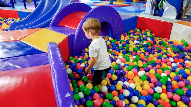 Foto di un ragazzino che gioca in piscina piena di palline di plastica colorate. Bambino che si diverte nel parco giochi nel centro commerciale