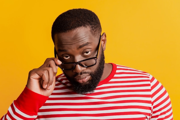 Foto di un ragazzo africano con la faccia seria che si toglie gli occhiali su sfondo giallo