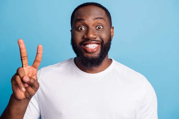 Foto di un ragazzo amichevole con un sorriso raggiante e sorridente che mostra il segno a V su sfondo blu