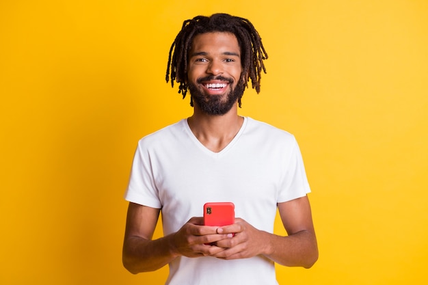 Foto di un simpatico ragazzo dalla pelle scura che tiene in mano un dispositivo telefonico sorridente a trentadue denti sfondo di colore giallo isolato