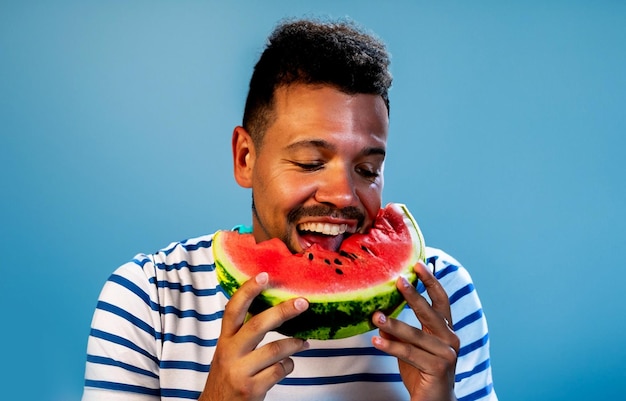 foto di un uomo bello felice che mangia un cocomero sullo sfondo blu