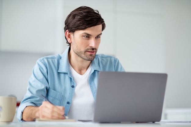 Foto di un uomo d'affari che naviga nel taccuino si siede al tavolo e guarda il webinar al chiuso