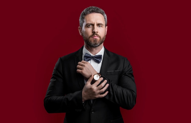 foto di un uomo in tuxedo in abito formale e orologio da braccio un uomo in smoking formale isolato su sfondo rosso un uomo in Smoking in abbigliamento formale uno studio un uomo con un tuxedo con un papillon formale