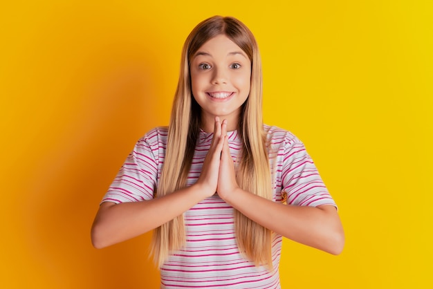 Foto di una bambina carina che tiene le mani imploranti isolate su sfondo giallo