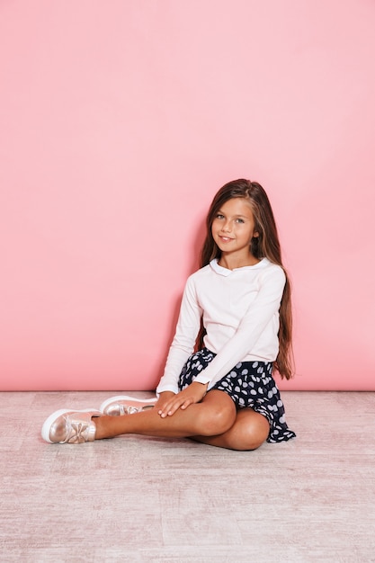 Foto di una bambina carina ottimista in posa isolata sul muro rosa seduto sul pavimento.