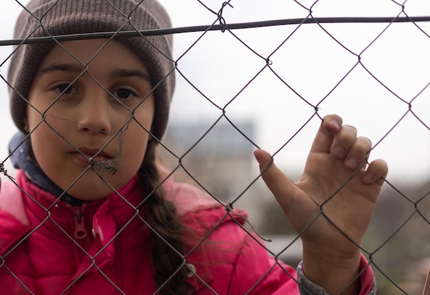 Foto di una bambina che tiene le sbarre. Bambina triste dietro le sbarre di ferro. Bambina dietro le sbarre. Concetto di violenza.