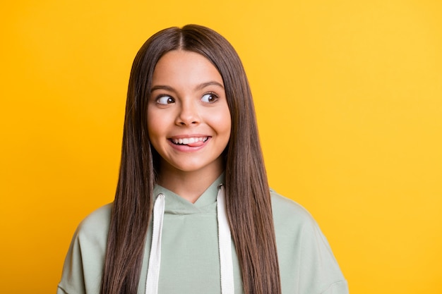 Foto di una bambina curiosa e divertente vestita con un abito verde casual che mostra la lingua che sembra uno spazio vuoto sorridente isolato sfondo di colore giallo