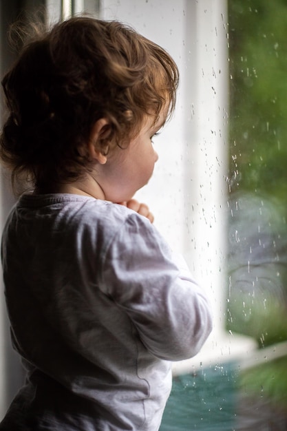 Foto di una bambina riccia sul davanzale della finestra, fuori dalla finestra piove