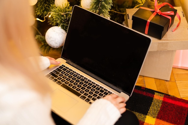 Foto di una bella donna bionda seduta su un divano che usa un laptop per fare acquisti per i regali di Natale.