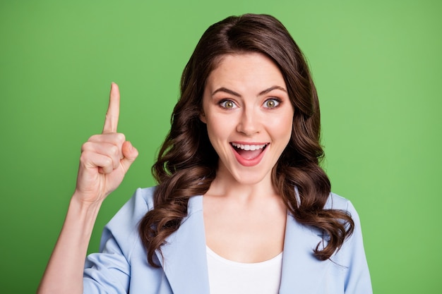 Foto di una bella donna con la pettinatura riccia alza il dito a bocca aperta indossa un blazer blu isolato sfondo di colore verde