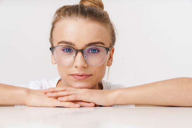 Foto di una bella donna contenta con gli occhiali che guarda la telecamera mentre si appoggia sul tavolo