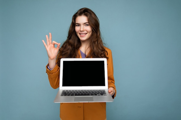 Foto di una bella giovane donna sorridente soddisfatta che tiene in mano un computer portatile che guarda la telecamera