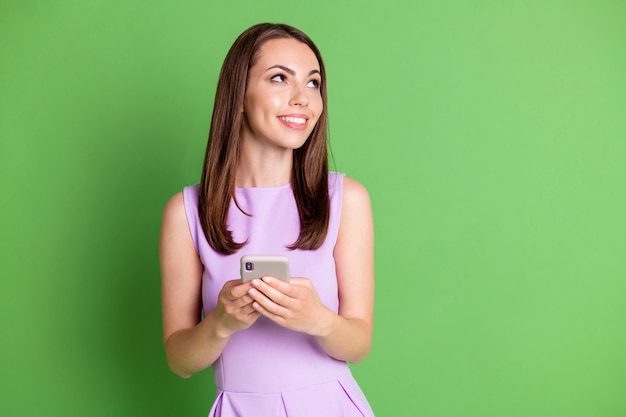 Foto di una bella ragazza sorridente ingannevole ragazza guardare spazio vuoto tenere smartphone creare contenuti blogger abbonato ripubblicare social media indossare abito viola isolato colore verde pastello sfondo