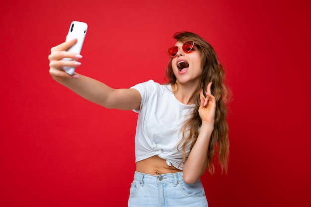 Foto di una bellissima giovane donna bionda che tiene in mano il telefono cellulare mentre fa una foto selfie usando