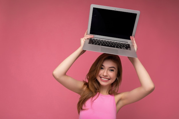 Foto di una bellissima giovane donna sorridente che tiene in mano un computer portatile che guarda la telecamera isolata sopra