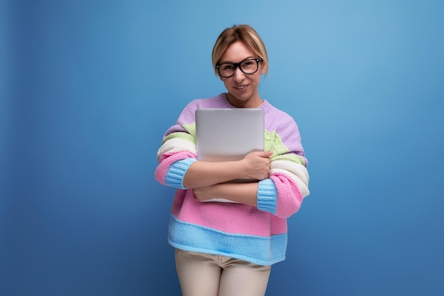 Foto di una carina e intelligente donna bionda freelance in maglione a righe con un portatile su sfondo blu con