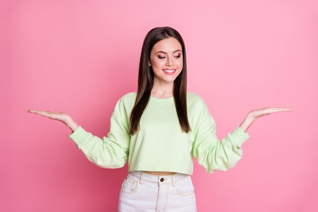 Foto di una donna attraente che tiene le braccia aperte con i palmi dello spazio vuoto che mostra prezzi di vendita interessanti due prodotti di novità per lo shopping indossano casual pullover verde raccolto jeans gonna isolato colore rosa sfondo