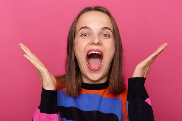 Foto di una donna caucasica allegra estremamente felice che indossa un maglione in posa contro il muro rosa urlando con espressione gioiosa e alzando le braccia sentendo un ottimo umore