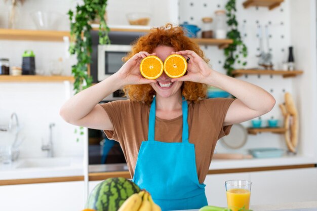 Foto di una donna caucasica carina che sorride e tiene due parti arancioni mentre cucina insalata di verdure nell'interno della cucina a casa