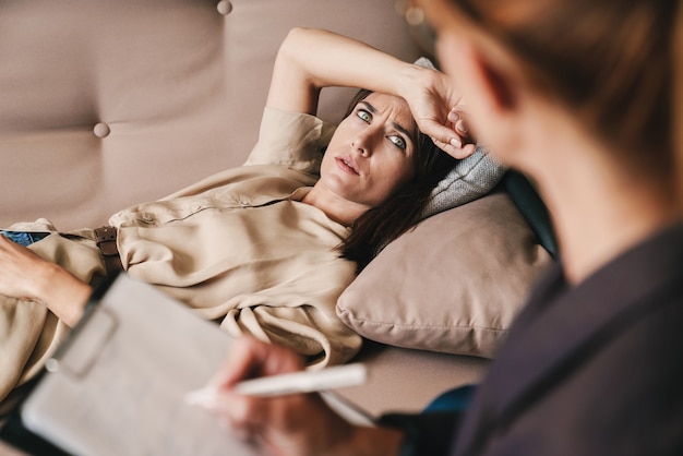 Foto di una donna caucasica confusa che ha una conversazione con uno psicologo durante una sessione di terapia in camera