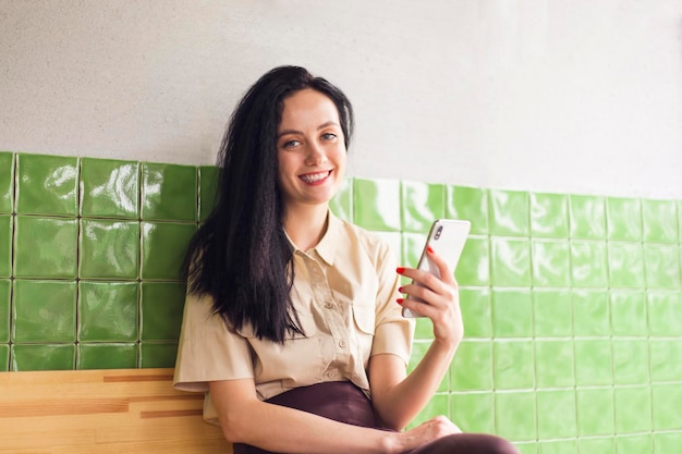 Foto di una donna felice e positiva vestita con una camicia beige che vende merci, gadget moderni, laboratorio interno.