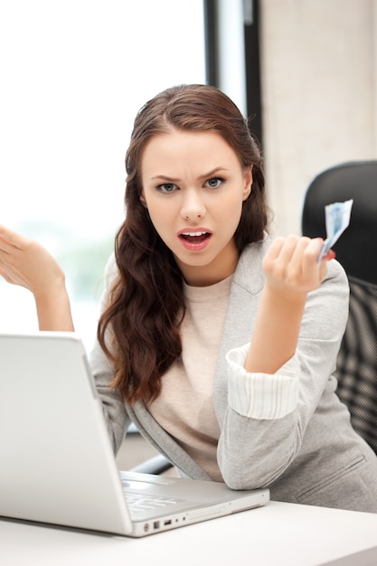 foto di una donna infelice con un computer portatile e denaro contante in euro