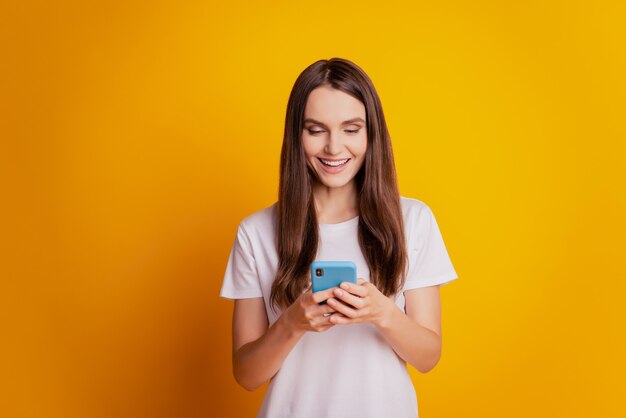 Foto di una donna pazza eccitata che tiene lo schermo del telefono che indossa una maglietta bianca in posa su sfondo giallo