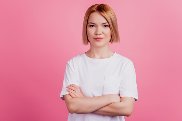 Foto di una donna sicura di sé con le mani incrociate che guarda la telecamera indossa una maglietta bianca isolata su sfondo rosa