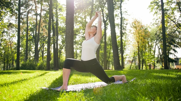 Foto di una donna sorridente felice di 40 anni che fa esercizi di yoga sul tappetino fitness nella foresta. Armonia della natura umana. Persone di mezza età che si prendono cura della salute mentale e fisica