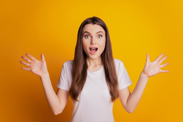Foto di una donna stupita e divertente che alza le mani con la bocca aperta indossa una maglietta bianca in posa su sfondo giallo