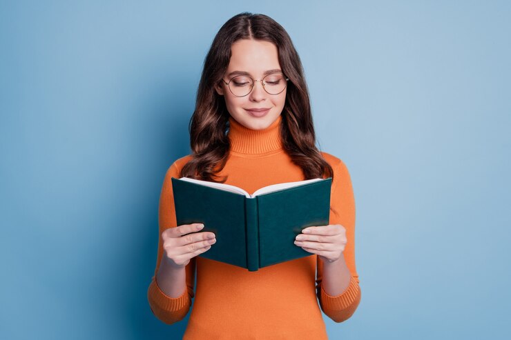 Foto di una donna tranquilla e sognante che legge il viso focalizzato sul libro in posa su sfondo blu