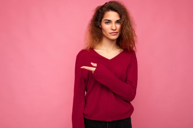 Foto di una giovane bella donna bruna ondulata con emozioni sincere che indossa un maglione rosa casual