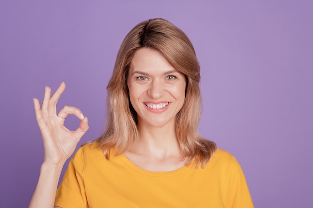 Foto di una giovane donna allegra felice sorriso positivo mostra ok bene segno affare fatto fresco isolato su sfondo di colore viola