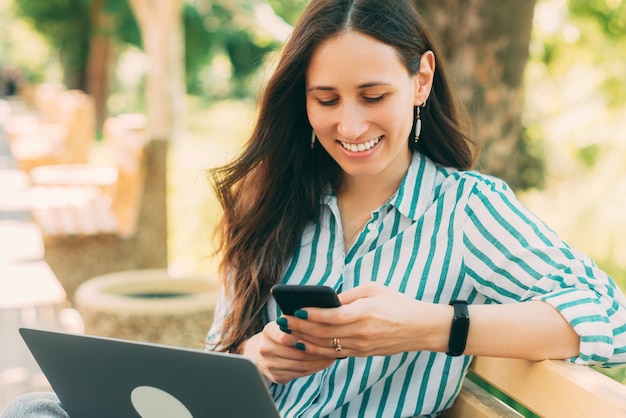 Foto di una giovane donna allegra in casual all'aperto digitando un messaggio o leggendo sullo smartphone