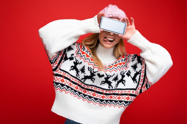 Foto di una giovane donna bionda sorridente attraente che indossa un cappello lavorato a maglia caldo e un maglione caldo invernale