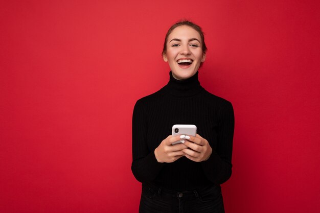 Foto di una giovane donna bruna positiva attraente che indossa un maglione nero in piedi isolata su red