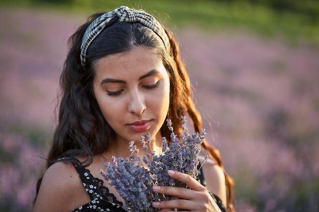 Foto di una giovane donna caucasica in abito che tiene in mano un mazzo di fiori, all'aperto attraverso il campo di lavanda in estate