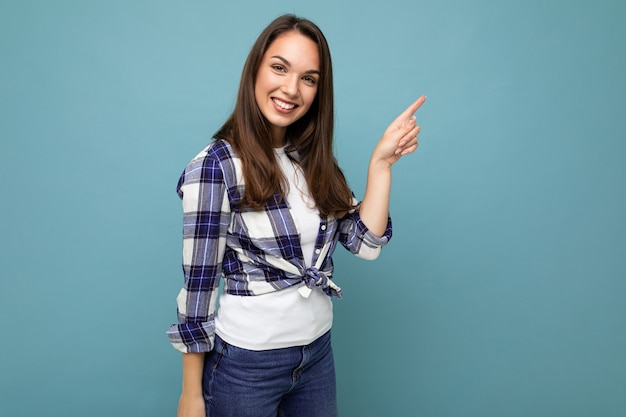 Foto di una giovane donna sorridente positiva attraente che punta il dito su copyspace che presenta annunci