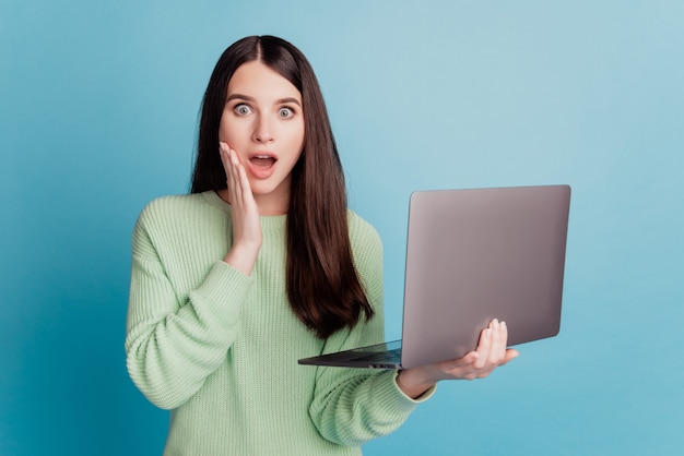 Foto di una giovane donna stupita che tiene un laptop isolato su sfondo blu
