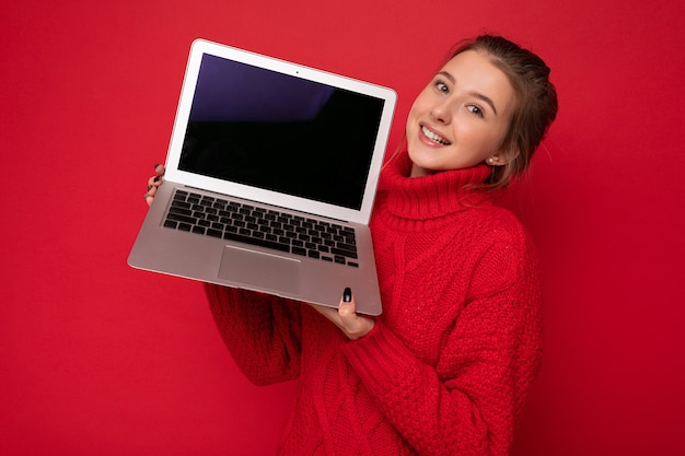 Foto di una giovane e bella donna che tiene in mano un computer portatile che guarda la telecamera isolata su un colorato