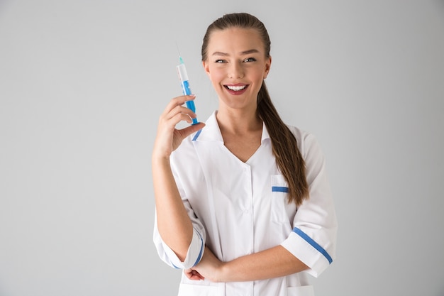 Foto di una giovane e bella donna cosmetologo medico isolato su muro grigio tenendo la siringa per iniezione