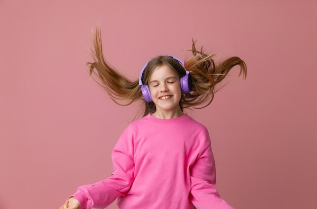Foto di una giovane ragazza adolescente carina e divertente in un maglione rosa con le cuffie che balla godendosi la musica su uno sfondo