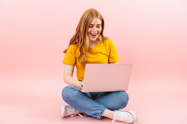 Foto di una giovane ragazza allegra sorridente positiva isolata sul muro rosa utilizzando il computer portatile.