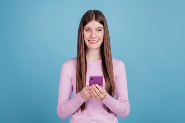 Foto di una giovane ragazza attraente, felice, sorriso positivo, leggere, sfogliare, utilizzare il cellulare isolato su uno sfondo di colore blu