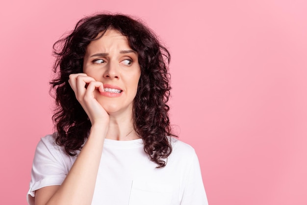 Foto di una giovane ragazza che morde i denti delle dita preoccupata spaventata sembra un problema di spazio vuoto isolato su uno sfondo di colore rosa