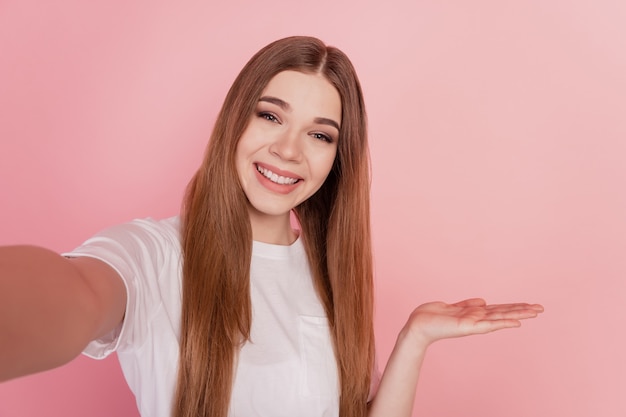 Foto di una giovane ragazza che spara selfie con la mano che tiene lo spazio vuoto sul muro rosa