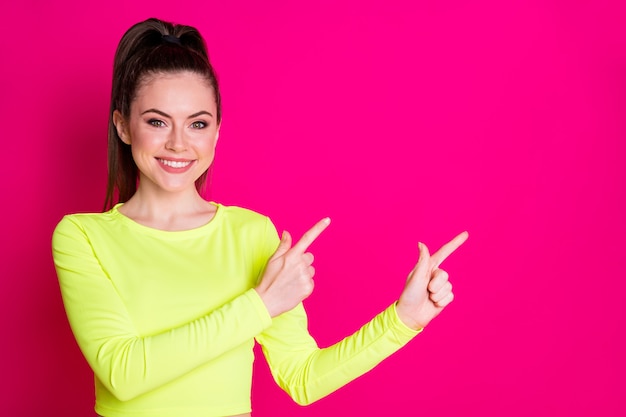 Foto di una giovane sportiva positiva che indica lo spazio vuoto del dito indice isolato su uno sfondo di colore rosa brillante