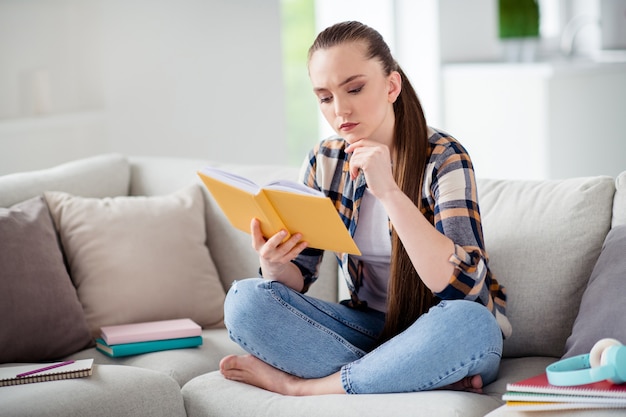 Foto di una giovane studentessa che tiene il diario del libro con le mani sul divano e le gambe incrociate sognanti